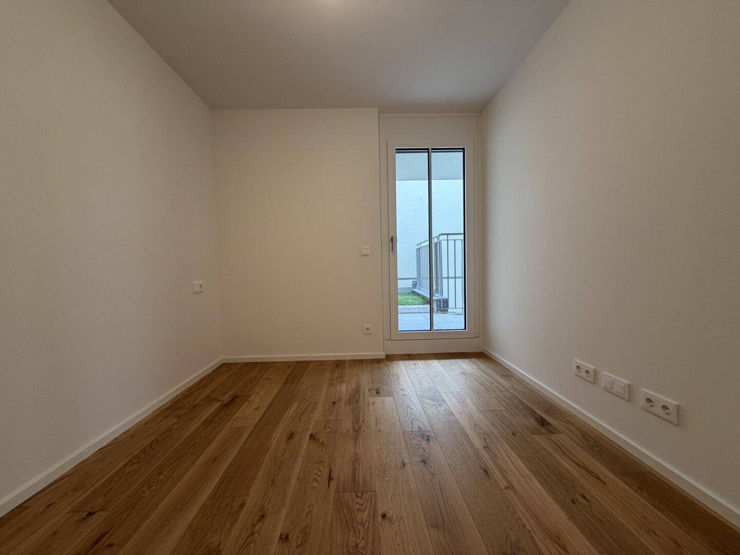 Leeres Zimmer mit Holzboden und Zugang zu einem kleinen Außenbereich.