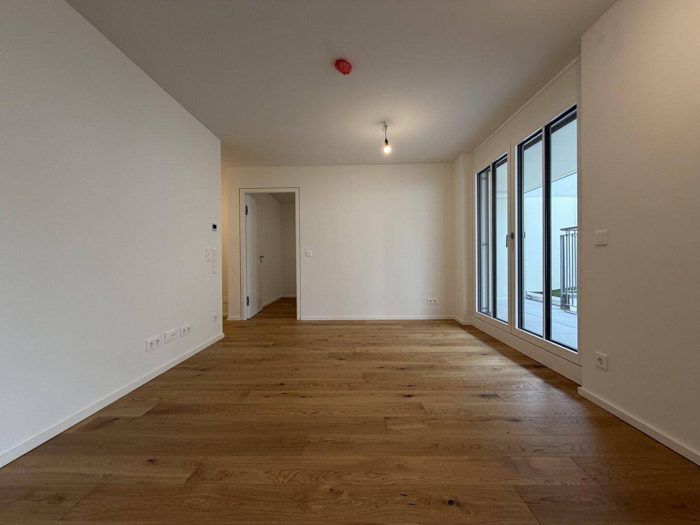 Heller Wohnraum mit Holzboden und großen Fenstern, die viel Tageslicht hereinlassen.