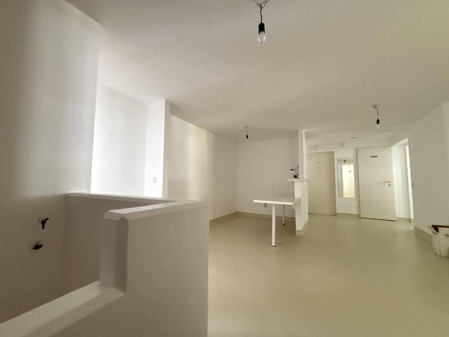 Heller, offener Raum mit weißen Wänden und einem kleinen Tresen, ideal für ein Büro oder Studio.