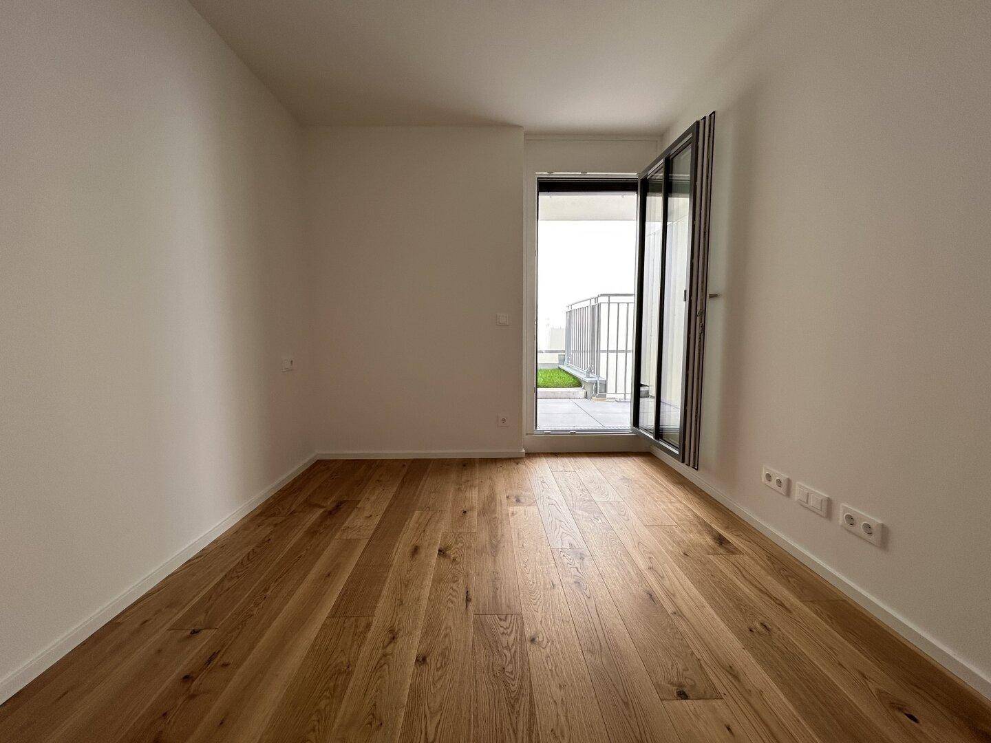 Helles Zimmer mit Holzboden und direktem Zugang zu einem Außenbereich, ideal als Schlafzimmer.