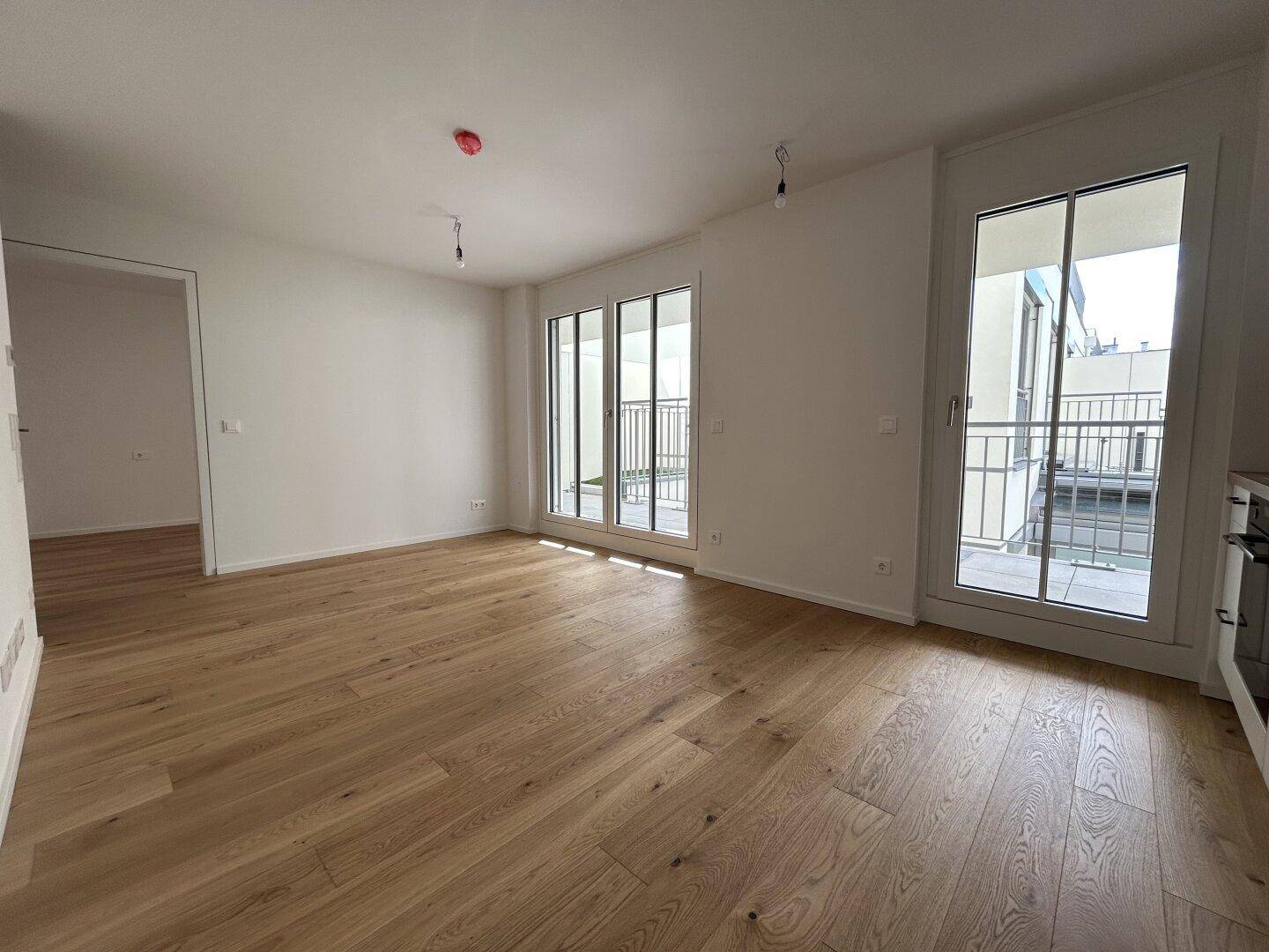 Lichtdurchfluteter Wohnbereich mit Eichenparkett und Zugang zu einem weiteren Zimmer und Balkon.
