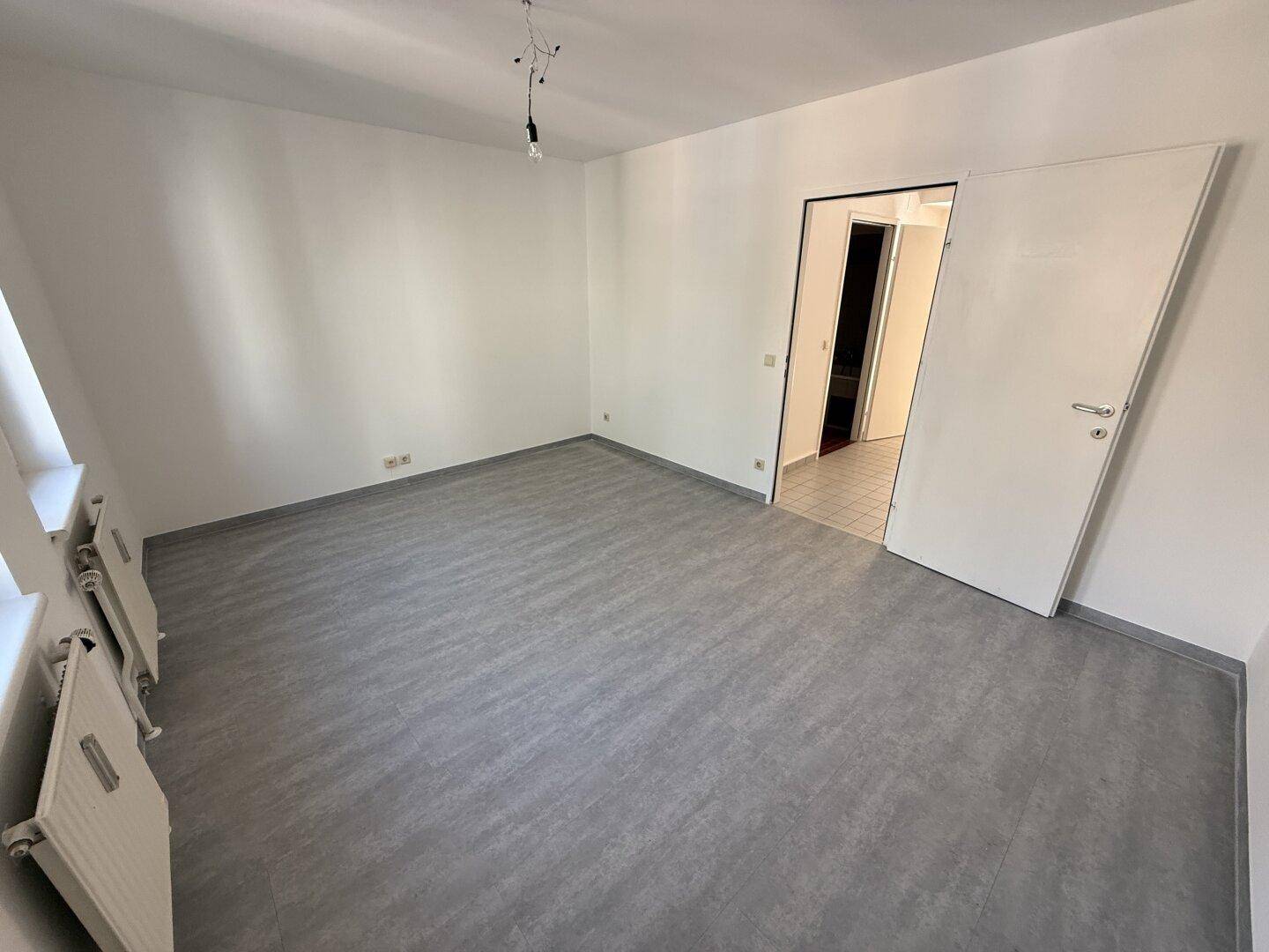 Unmöblierter Raum mit grauem Vinylboden und weiß gestrichenen Wänden, bereit für die individuelle Gestaltung.
