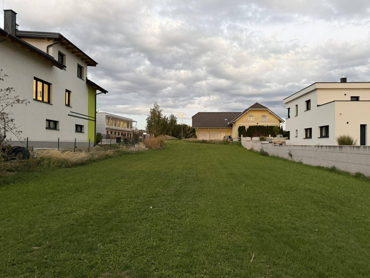 Grüne Rasenfläche umgeben von verschiedenen Wohnhäusern unter einem bewölkten Himmel.