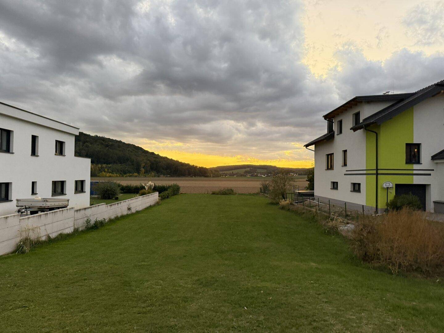 Weitläufige Rasenfläche zwischen zwei modernen Häusern mit Blick auf einen malerischen Sonnenuntergang.
