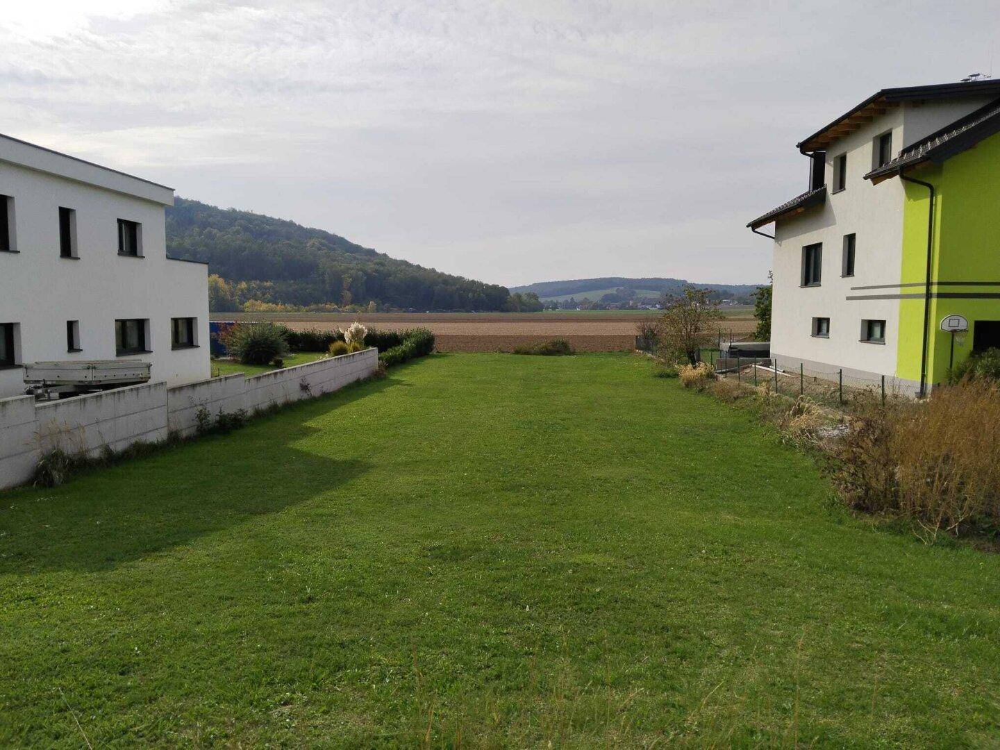 Großes grünes Grundstück zwischen zwei Gebäuden mit weitem Blick auf Felder und Hügel.