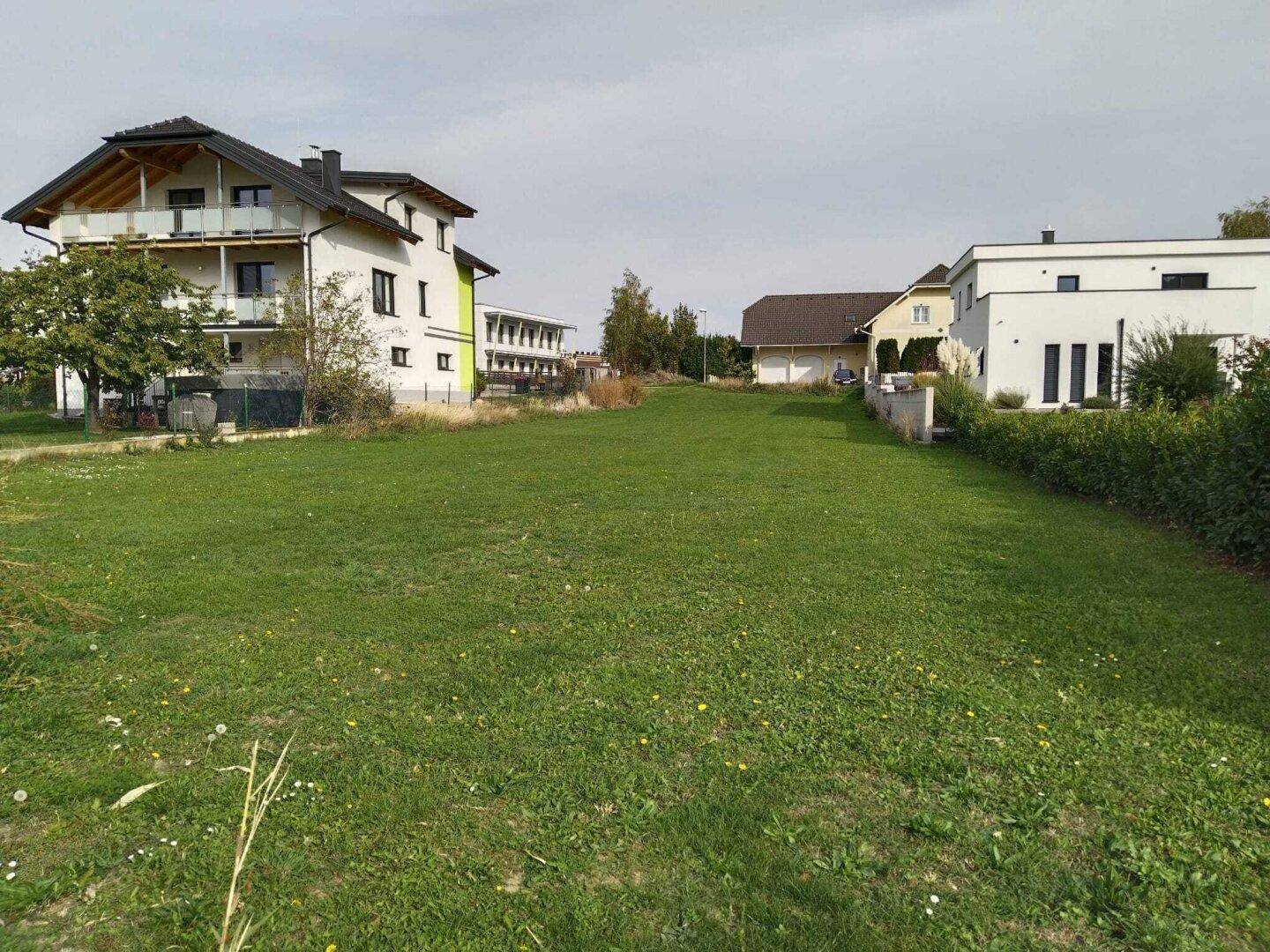 Weitläufiges grünes Grundstück umgeben von modernen Wohngebäuden mit Balkonen und ländlicher Aussicht.