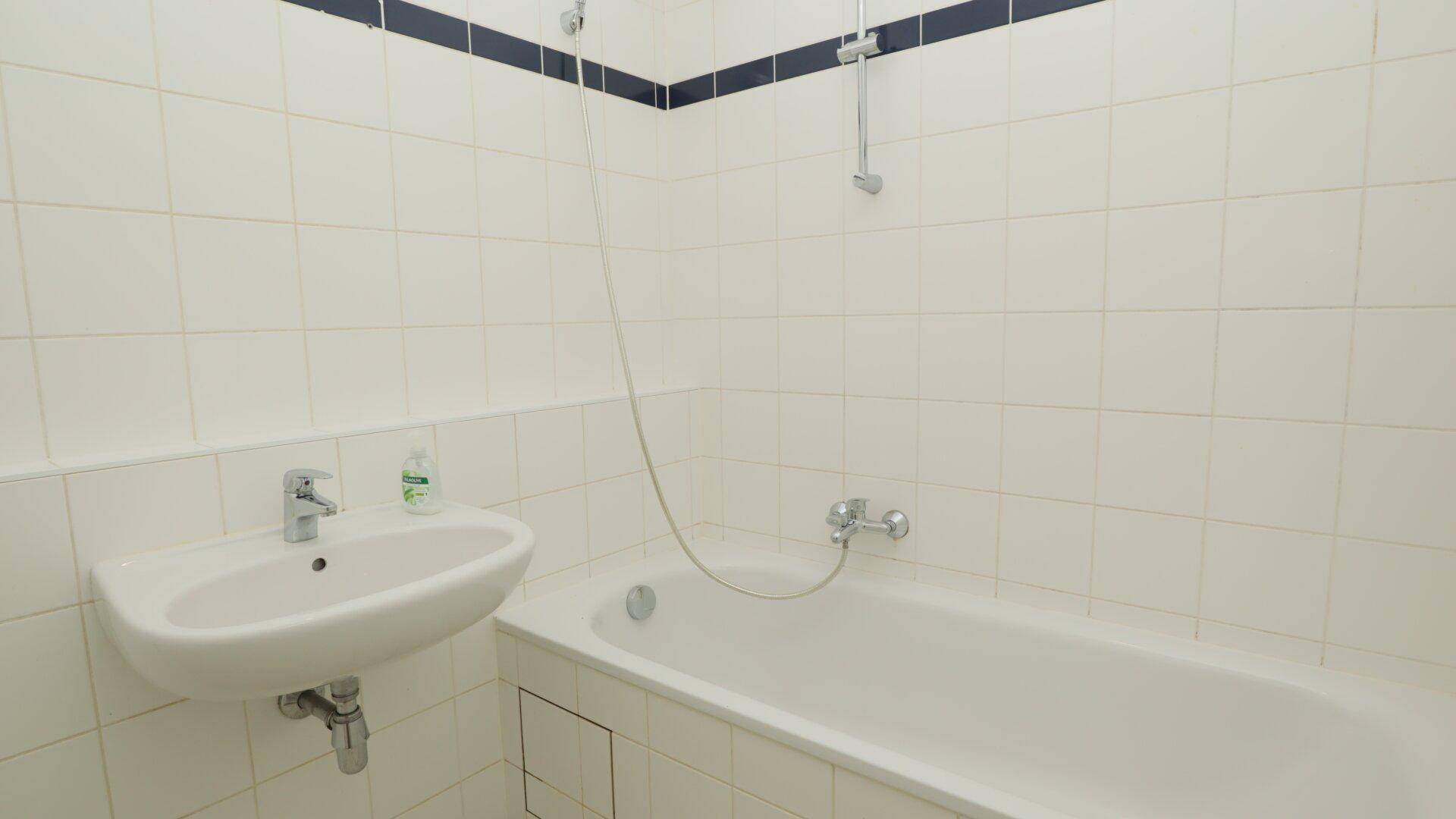 Funktionales Badezimmer mit Badewanne, Waschbecken und weißen Fliesen, typisch für die 80er Jahre.
