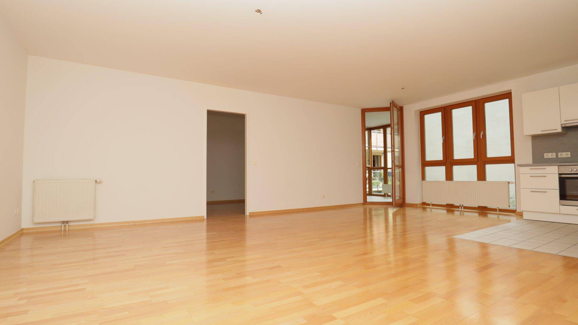Heller, offener Wohn- und Essbereich mit Parkettboden und Zugang zu einem Balkon.