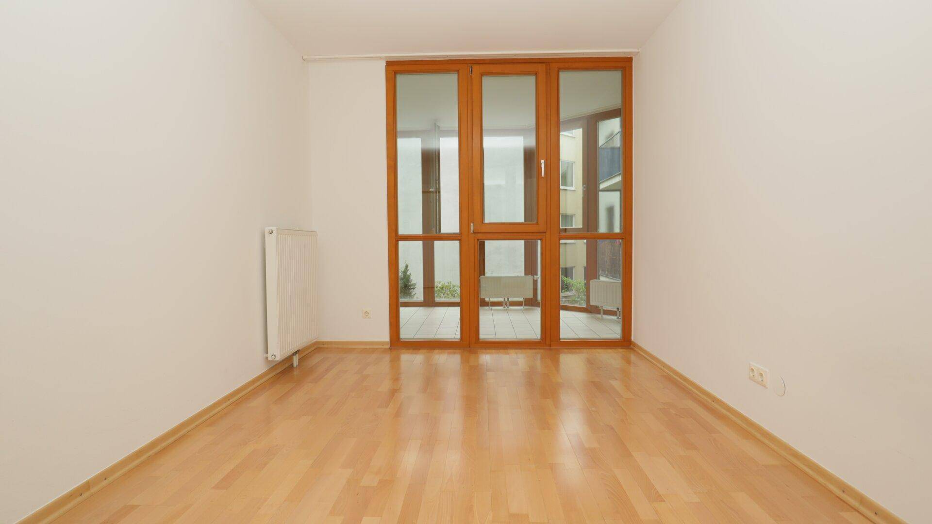 Leeres Zimmer mit Parkettboden und großen Fenstern, die viel Tageslicht hereinlassen.
