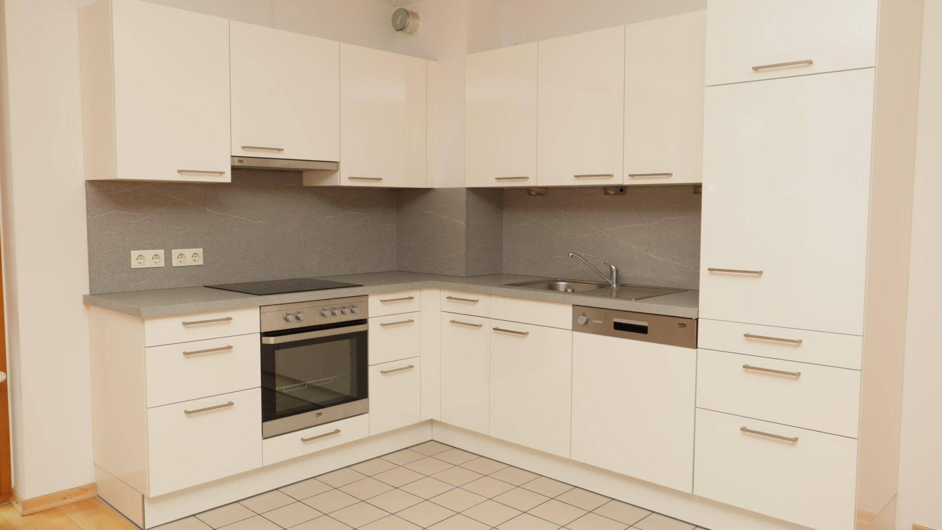 Moderne Einbauküche mit weißen Hochglanzfronten, integrierten Geräten und Fliesenboden.