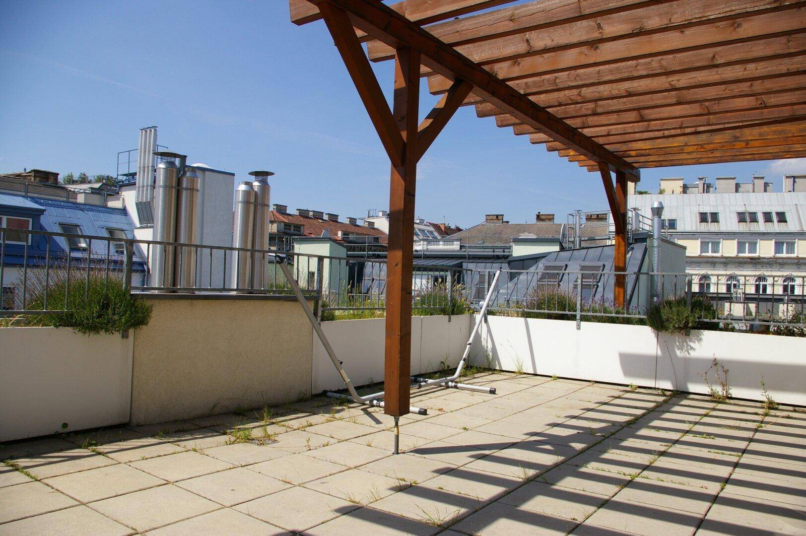 Geräumige Dachterrasse mit Holzpergola und Blick über die Dächer der Stadt.