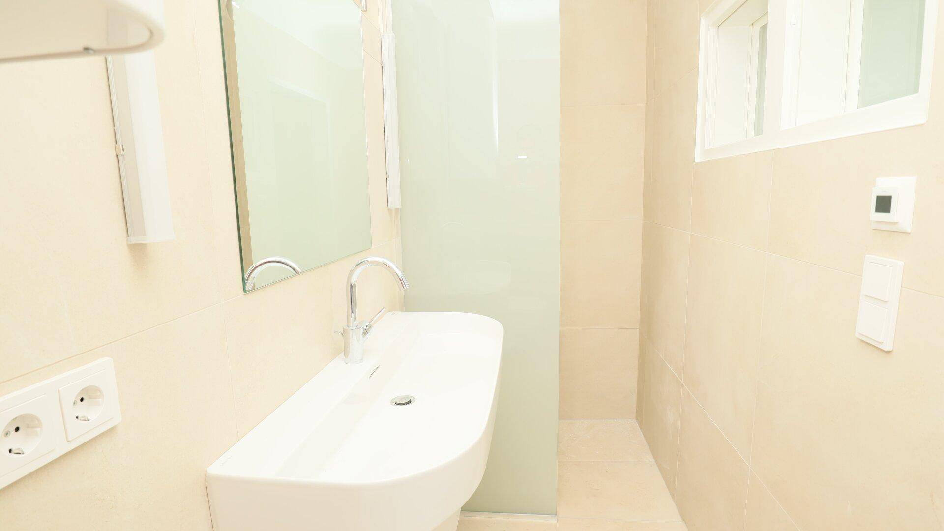 Modernes Badezimmer mit hellem Fliesenboden, elegantem Waschbecken und Spiegelschrank.