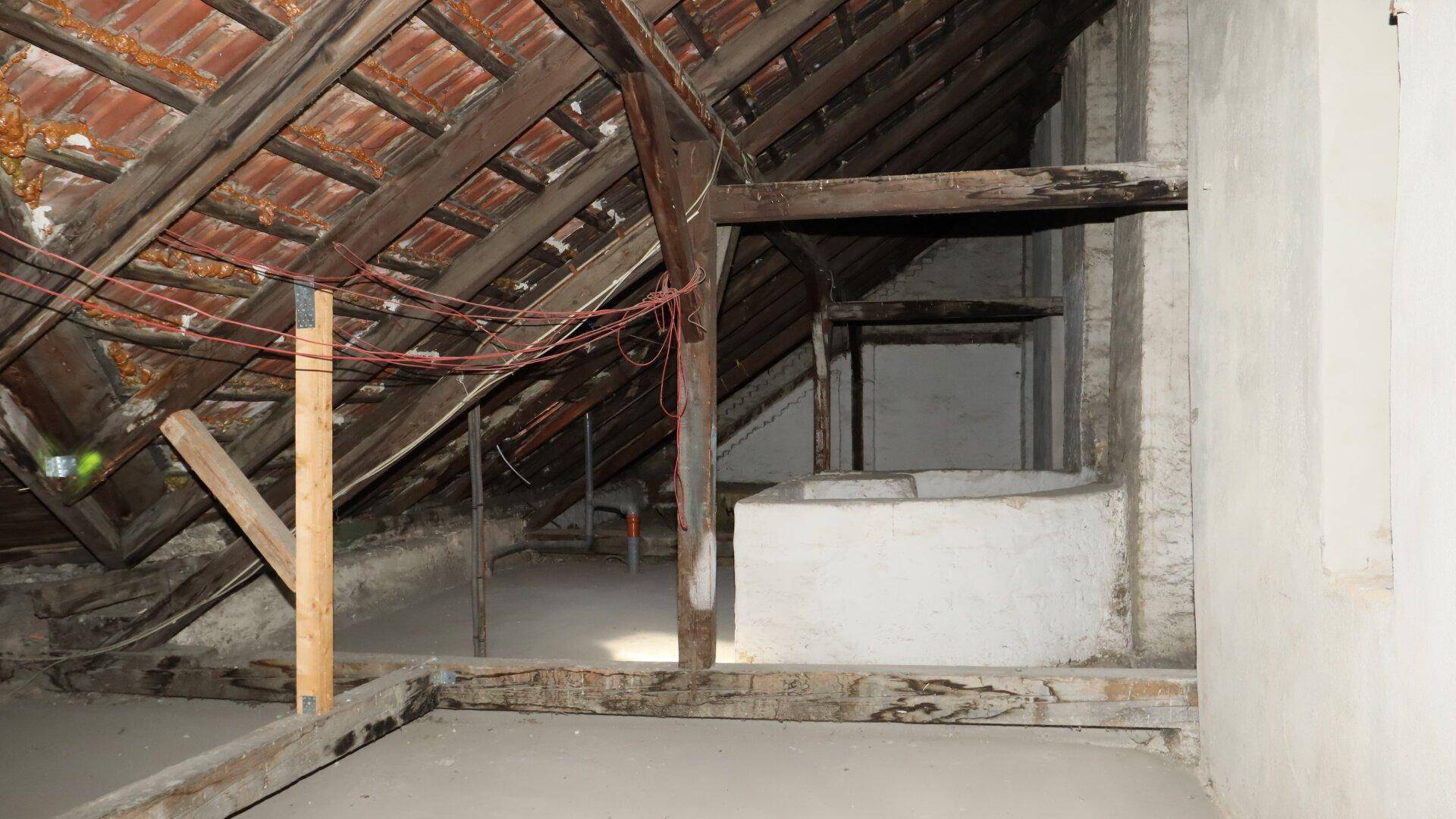 Rohbau-Dachboden mit freiliegenden Holzbalken und einem kleinen Fensterbereich.