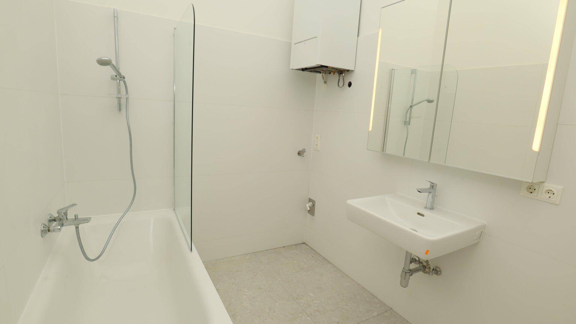 Helles Badezimmer mit Badewanne, Dusche, modernem Waschbecken und Spiegelschrank.
