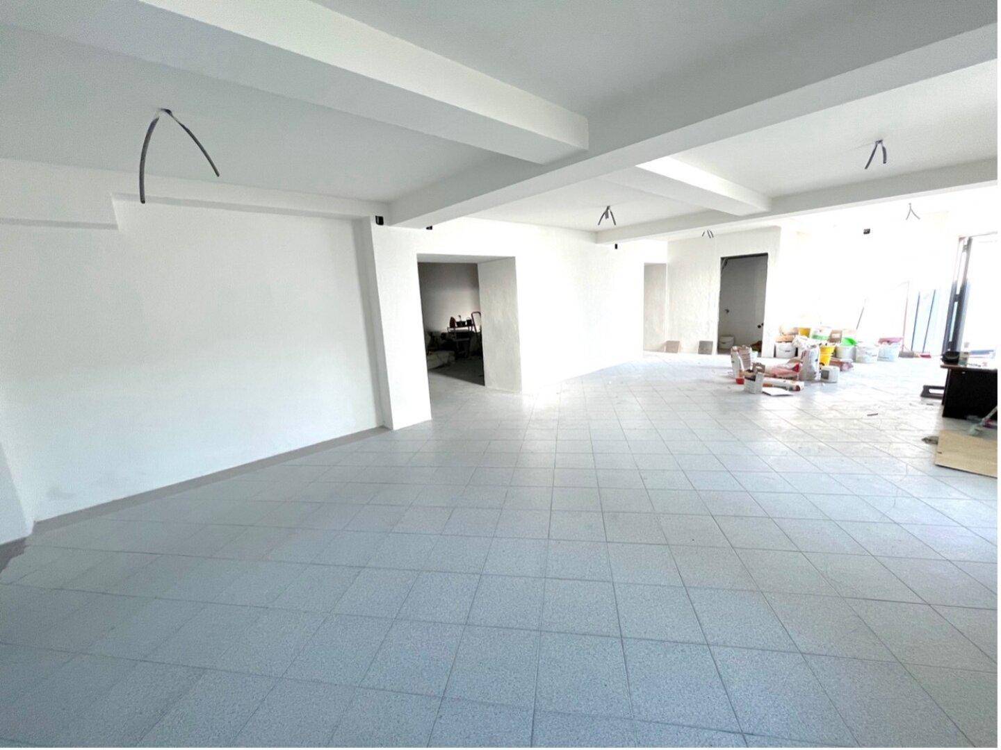 Leere Gewerbefläche mit Fliesenboden und sichtbaren Deckeninstallationen, bereit für den Ausbau.