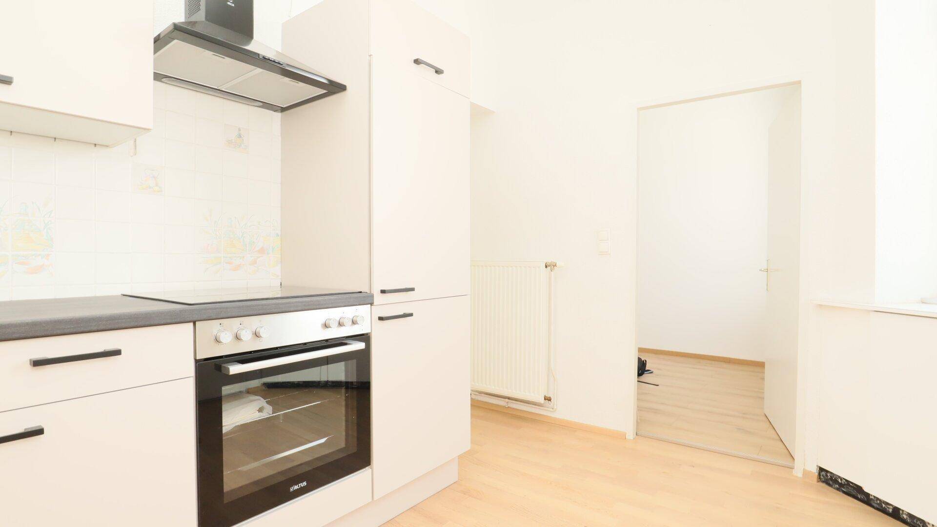 Moderne Küche mit hellen Schränken, Backofen, Induktionskochfeld und Dunstabzugshaube.