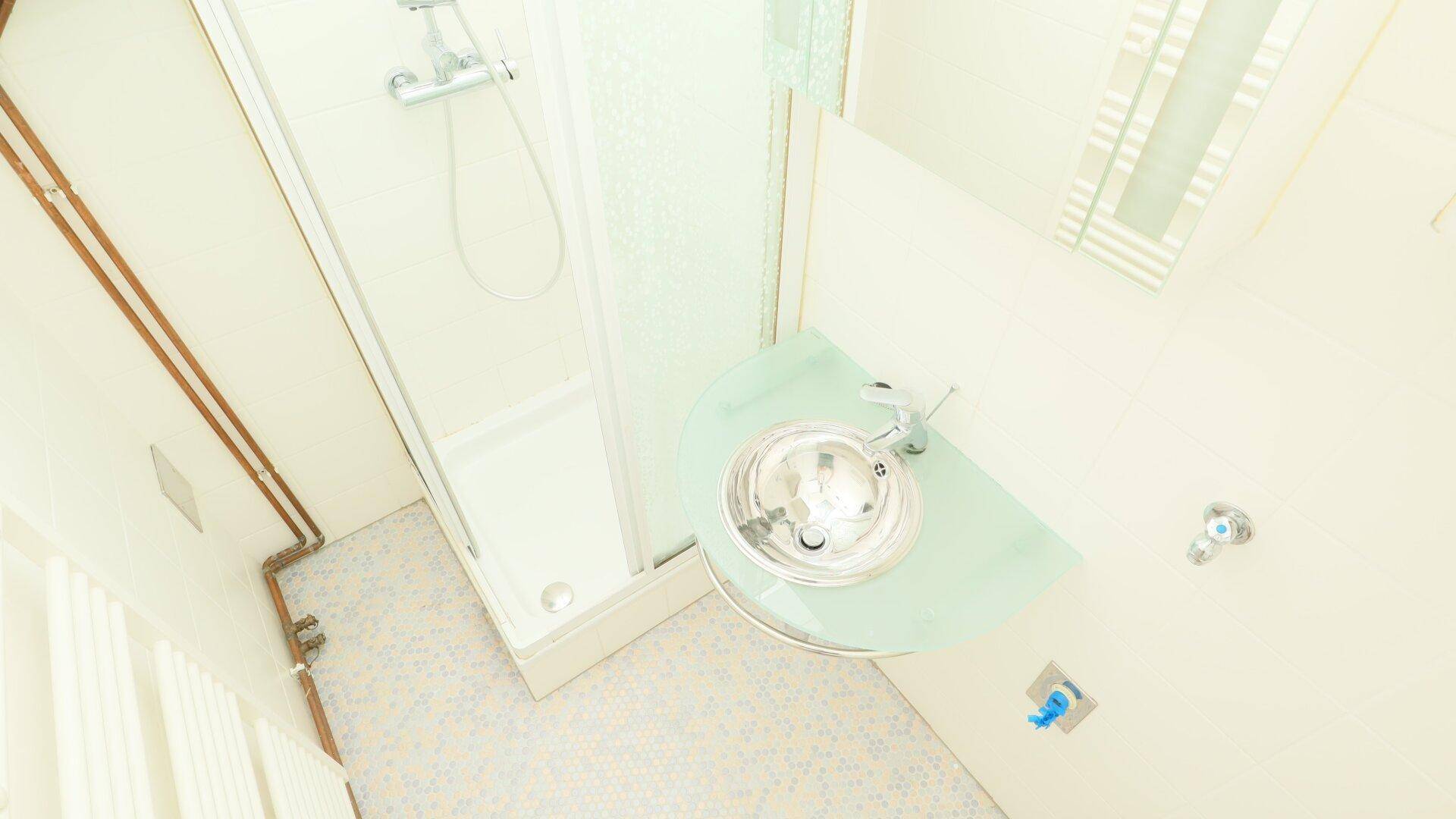 Helles Badezimmer mit Duschkabine und modernem Einzelwaschbecken, ausgestattet mit Fliesenboden.