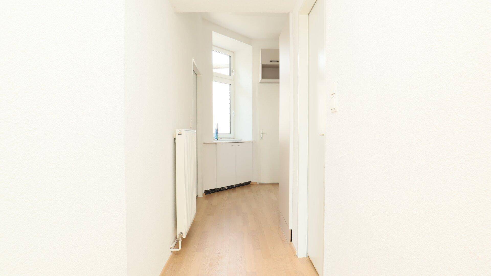 Heller Flur mit Holzfußboden, der zu einem Fenster am Ende führt.
