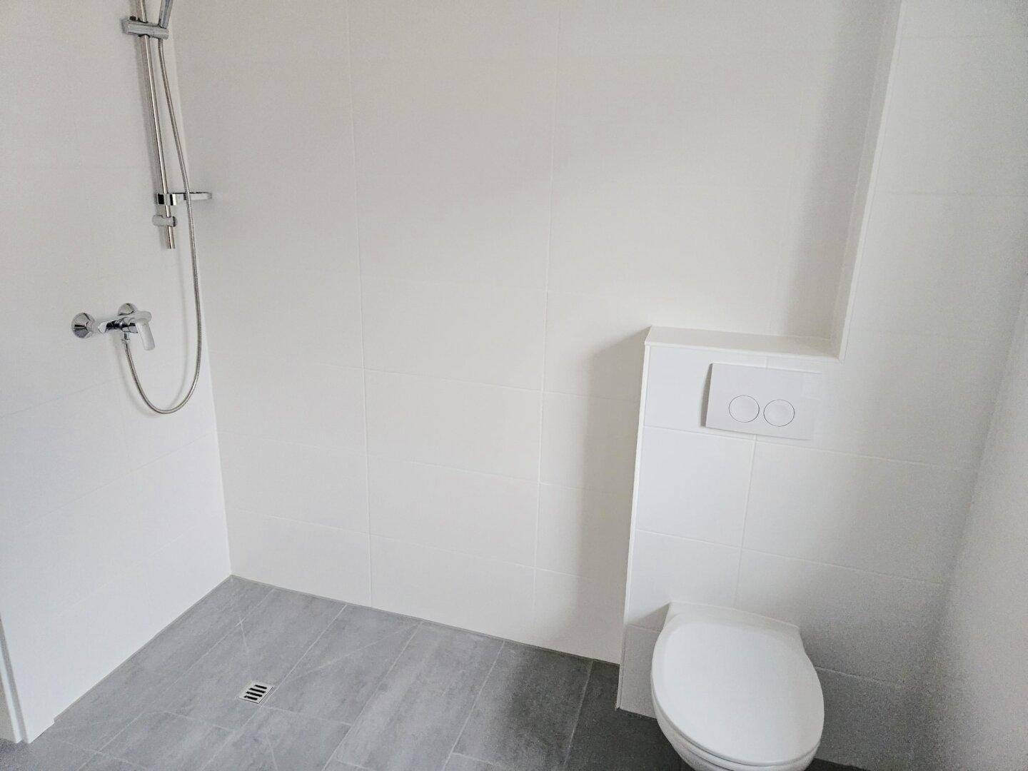 Helles Badezimmer mit Duschbereich, wandhängendem WC und modernen Fliesen in Weiß und Grau.