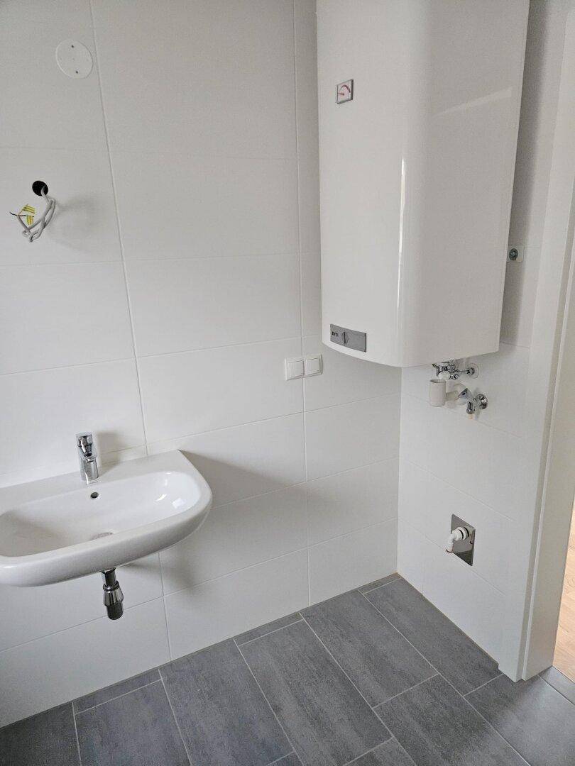 Funktionales Badezimmer mit Waschbecken, weißen Fliesen und einem wandmontierten Warmwasserbereiter.