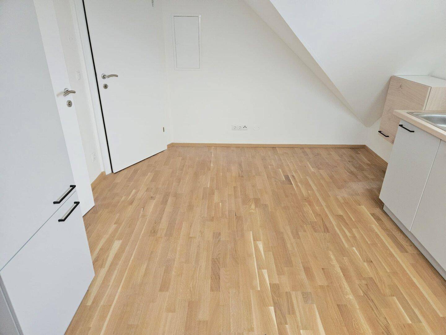 Leerer Raum mit hellem Holzboden, weißen Wänden und Dachschrägen, bereit zur individuellen Gestaltung.