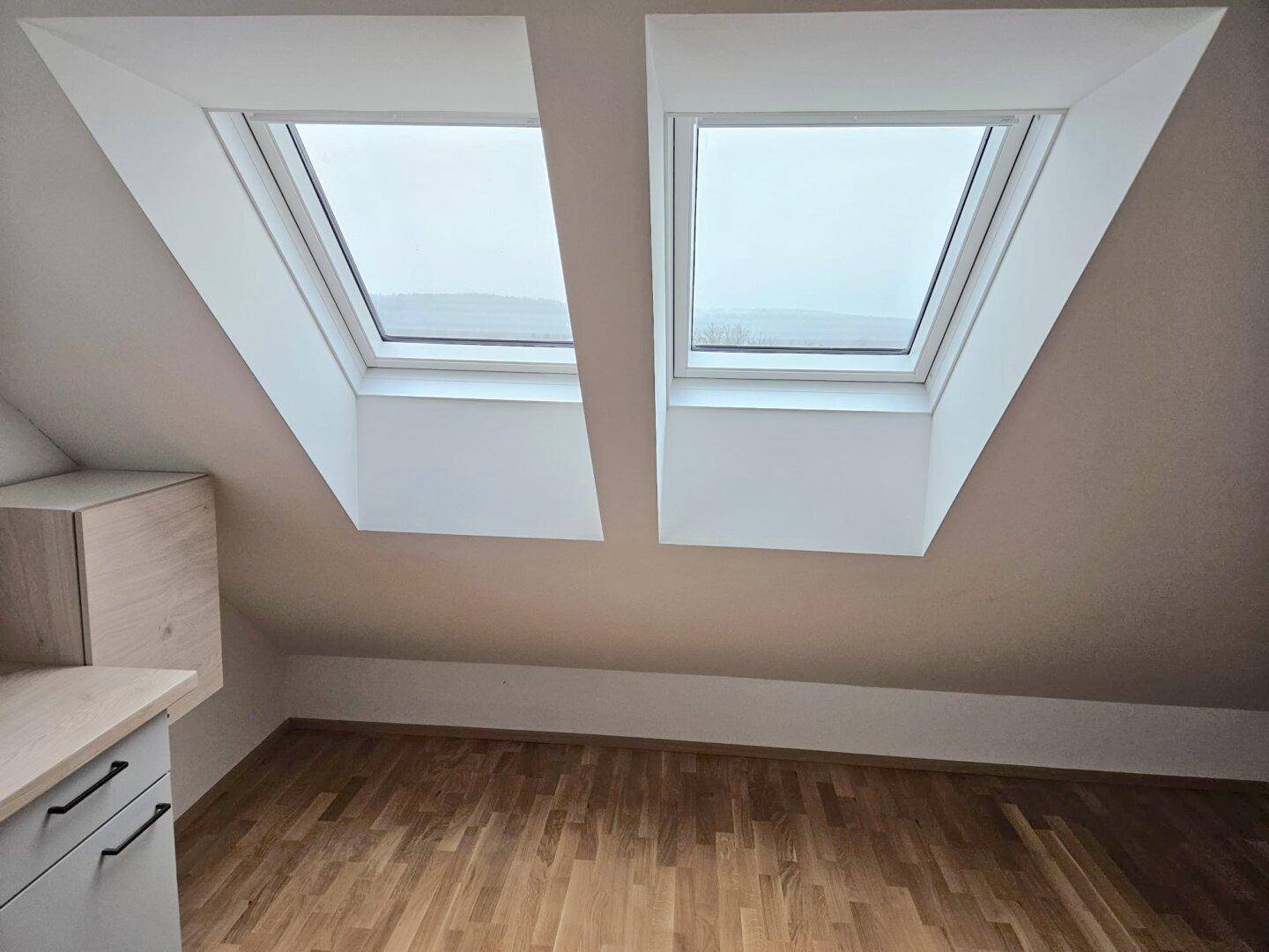 Heller Raum mit zwei Dachfenstern, Holzboden und Dachschrägen, bietet viel natürliches Licht.