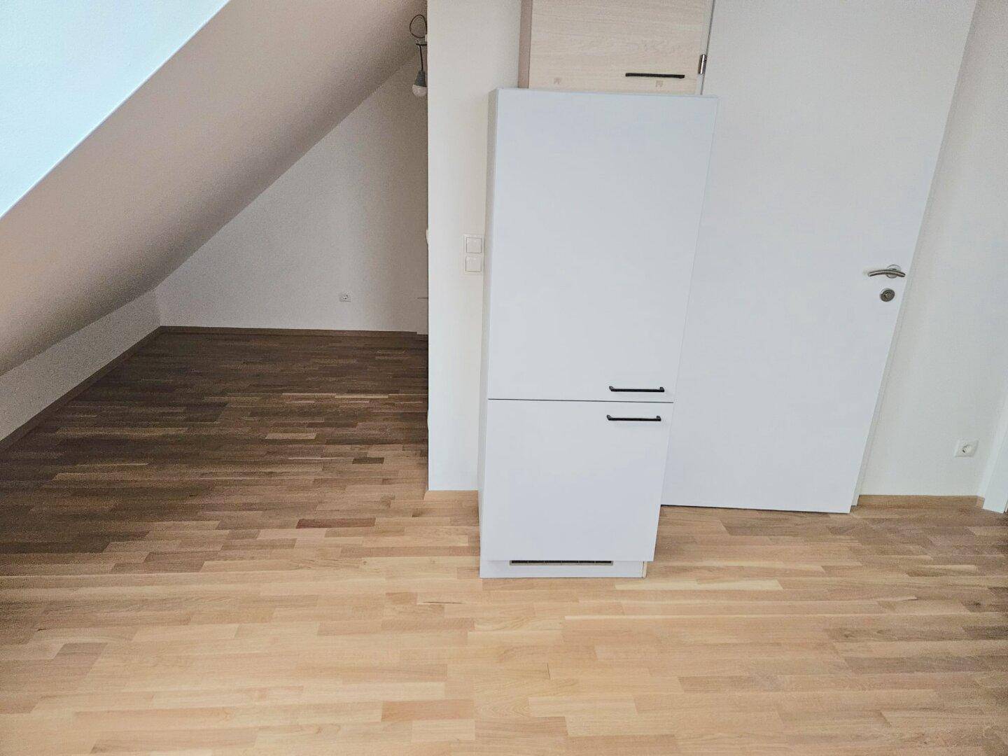 Geräumiger, leerer Raum mit Holzboden, weißen Wänden und Dachschrägen, ideal für flexible Nutzung.