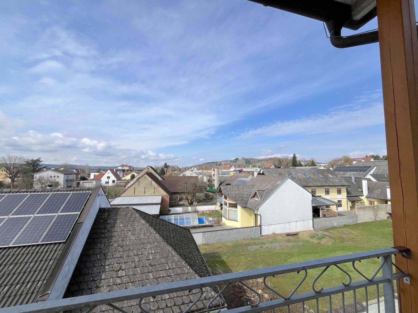 Balkonblick über die Dächer der Nachbarschaft mit Solaranlagen und einem kleinen Pool im Garten.