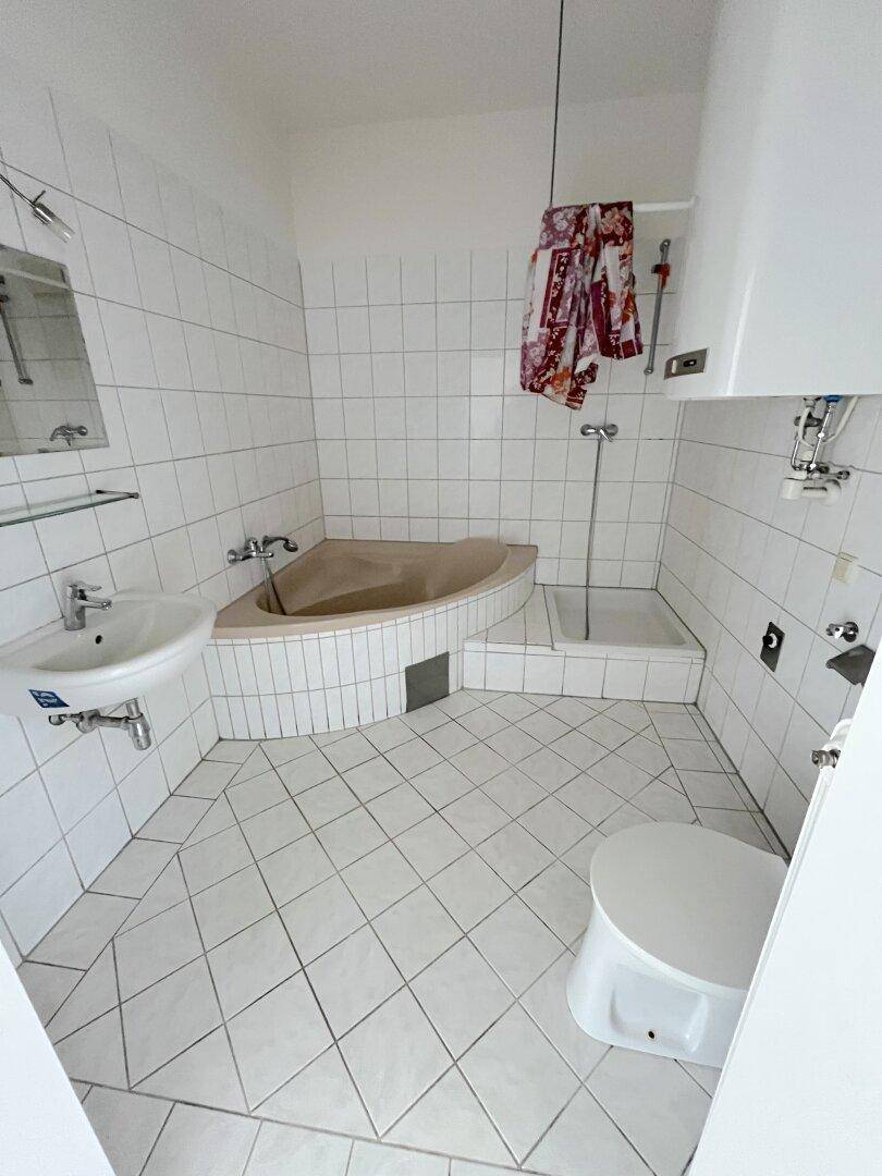 Badezimmer mit weißen Fliesen, Eckbadewanne, separater Dusche, Toilette und Waschbecken.
