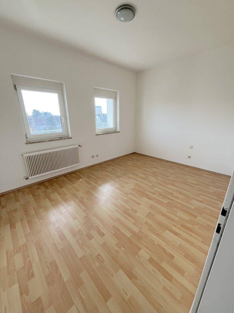 Helles Schlafzimmer mit Laminatboden, weißen Wänden und zwei Fenstern für viel Tageslicht.