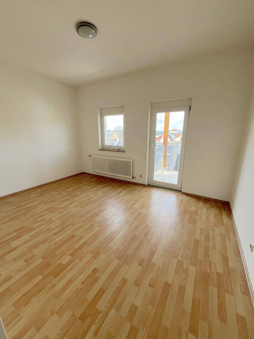 Leeres Schlafzimmer mit hellem Laminatboden, weißen Wänden und direktem Zugang zum Balkon.