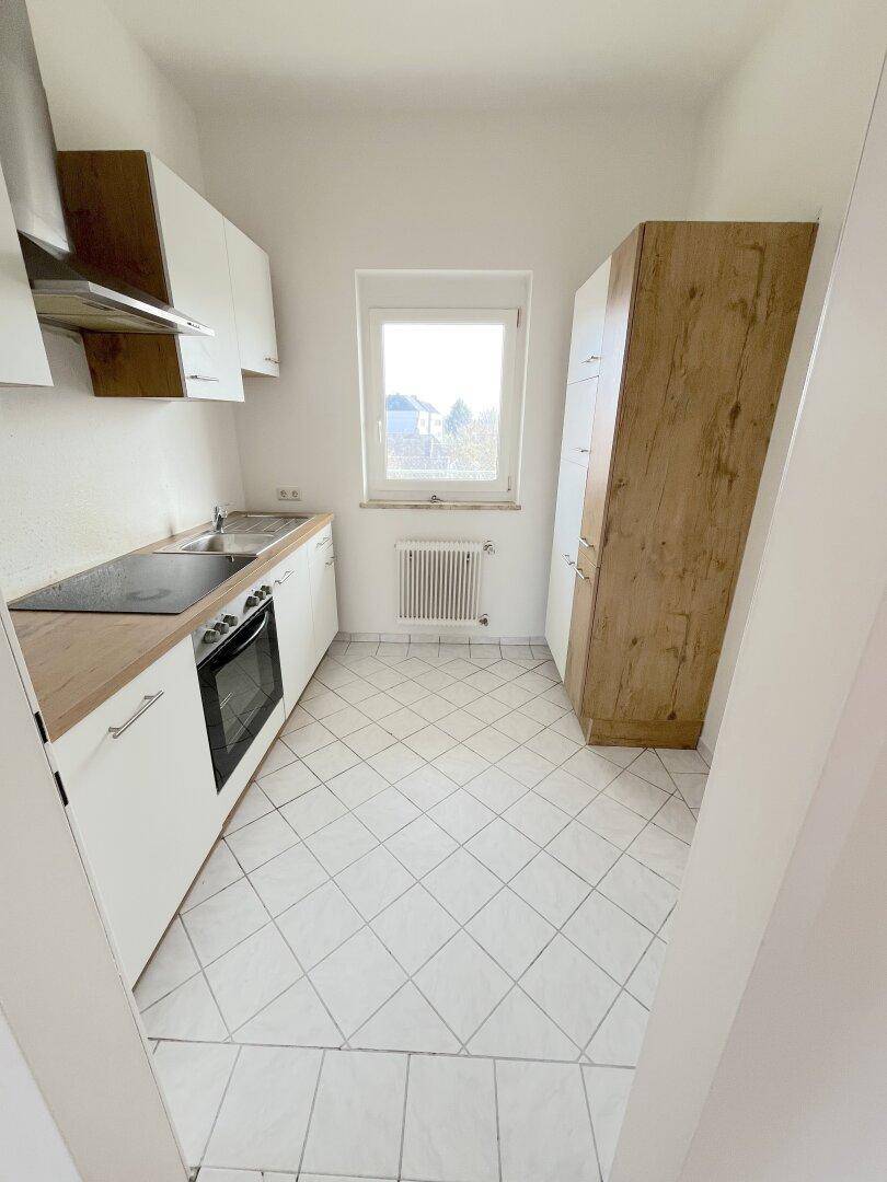 Funktionale Küche mit weißen Fliesen, hellen Schränken, Holzarbeitsplatte und Fenster.