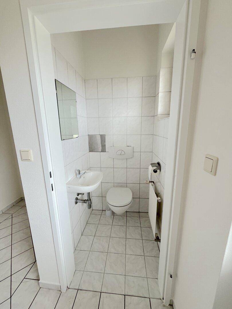 Kleines Gäste-WC mit weißen Fliesen an Boden und Wänden, Toilette und Handwaschbecken.