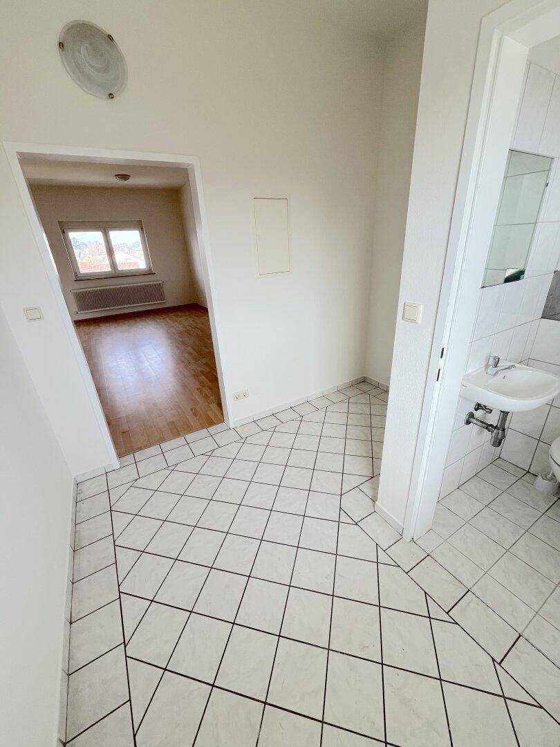 Fliesenboden im Flur mit Blick in ein Zimmer mit Laminat und ein kleines Badezimmer.