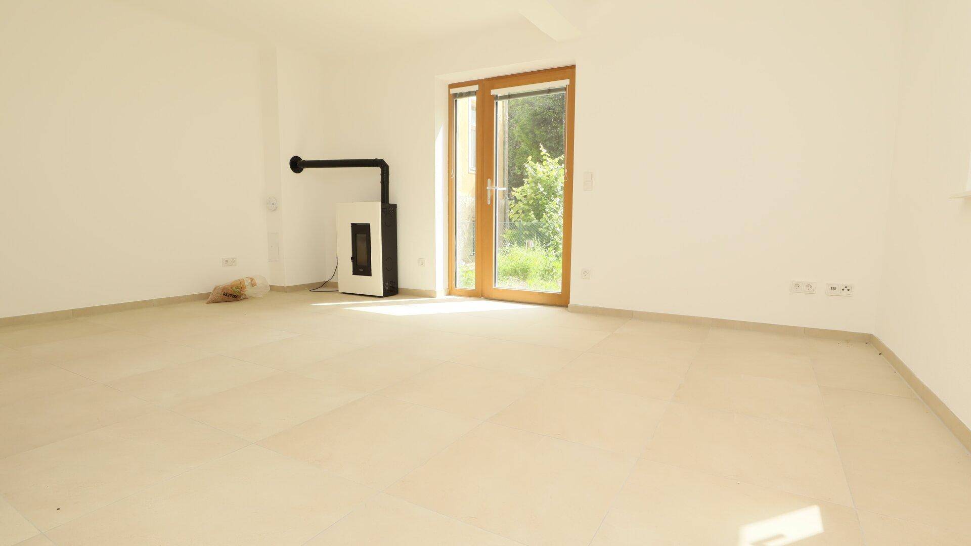 Heller Wohnraum mit modernem Kaminofen, großen Fenstern und Zugang zum Garten.