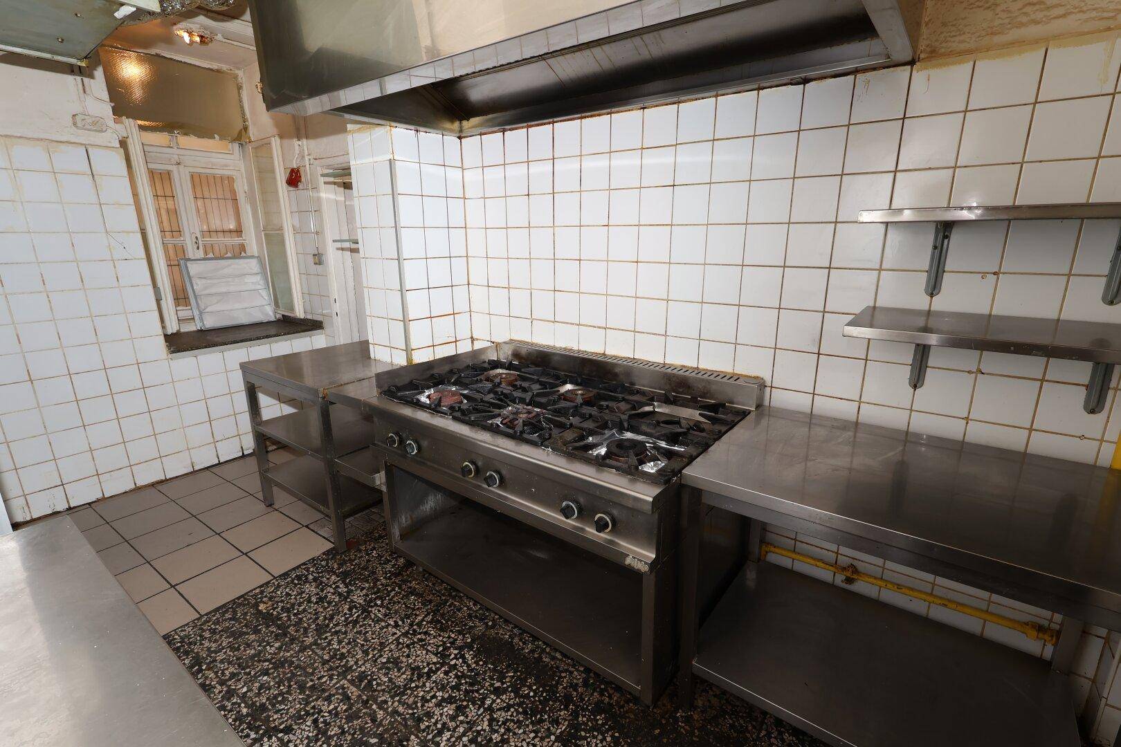 Gewerbliche Küche mit großem Gasherd, Edelstahlflächen und gefliesten Wänden, bereit für den Einsatz.