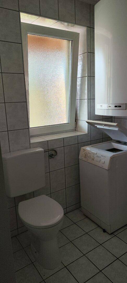 Badezimmer mit Toilette, Waschmaschine und Fenster für Belüftung und Tageslicht.