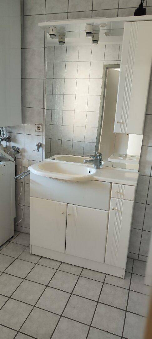 Badezimmer mit Waschtisch, Spiegel und hellen Fliesen an Wänden und Boden.