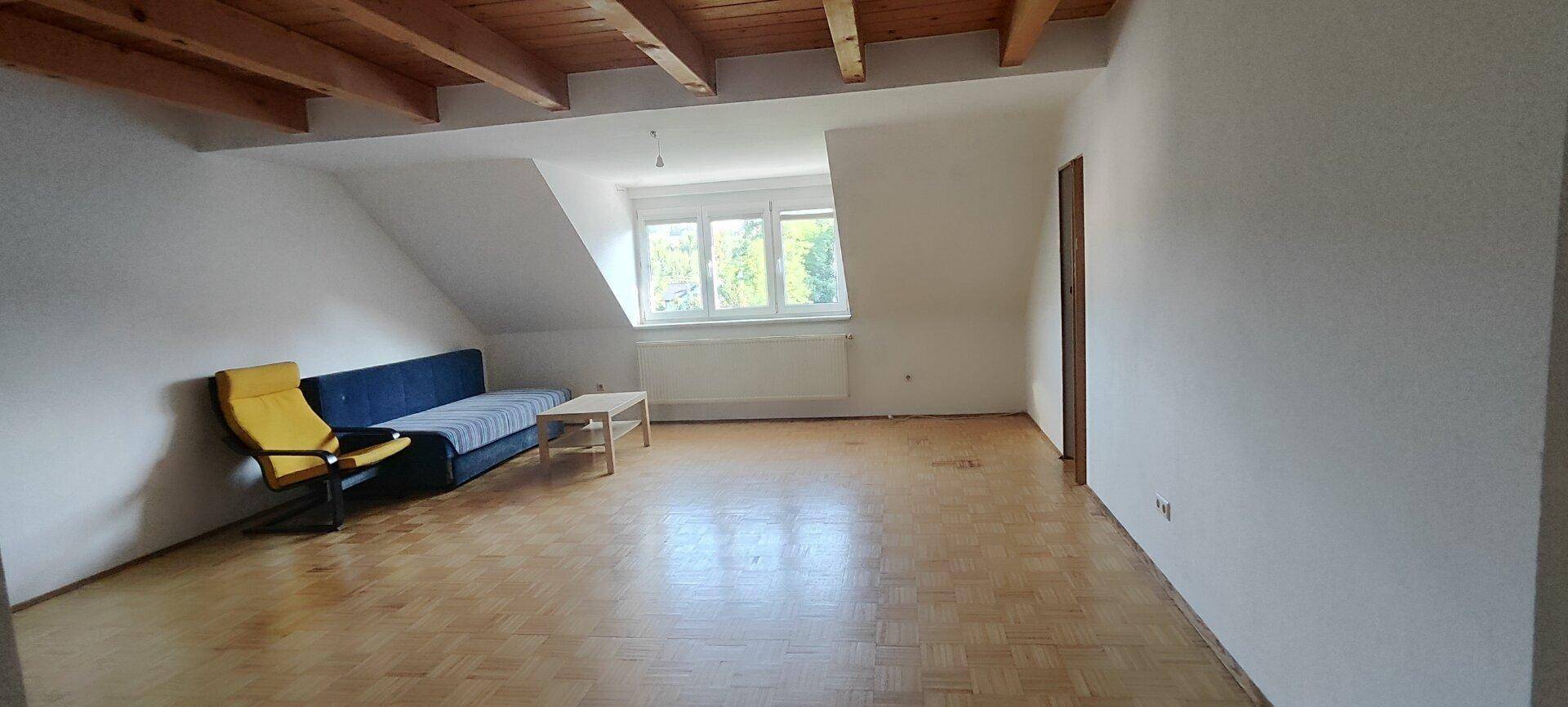 Helles Wohnzimmer im Dachgeschoss mit Schrägen, Parkettboden und einem großen Fenster.