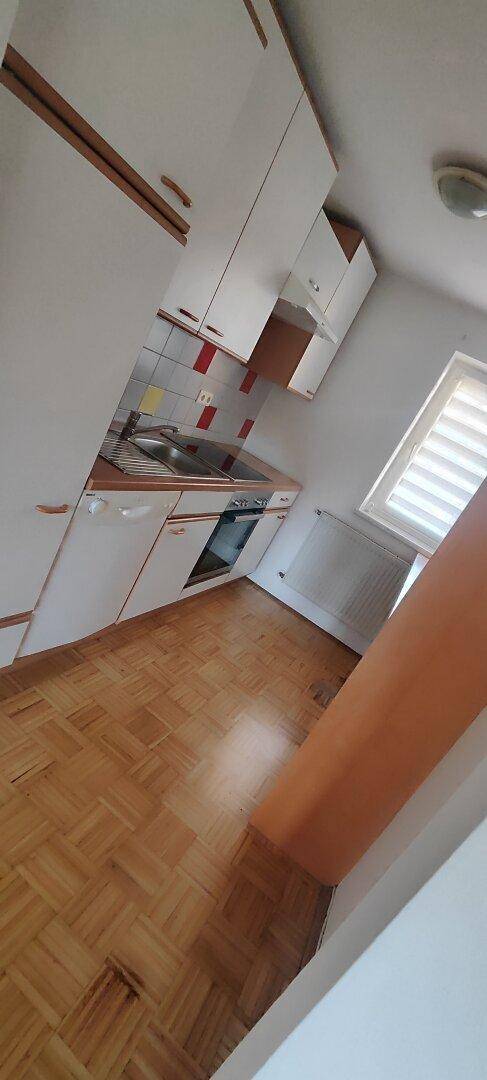 Kleine Küche mit weißen Schränken, Parkettboden und einem Fenster für natürliches Licht.