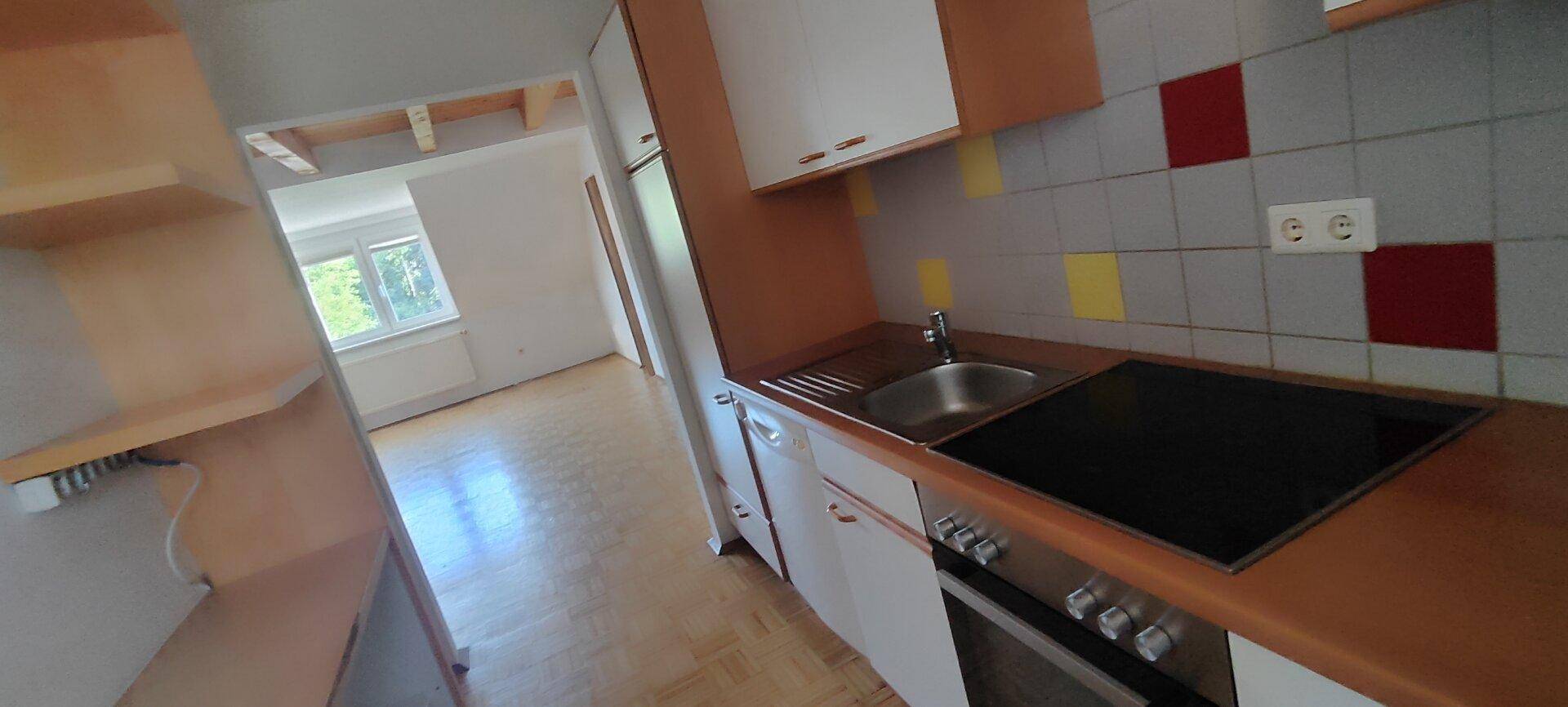 Detailansicht der Küche mit Spüle, Kochfeld und bunten Fliesen an der Wand.