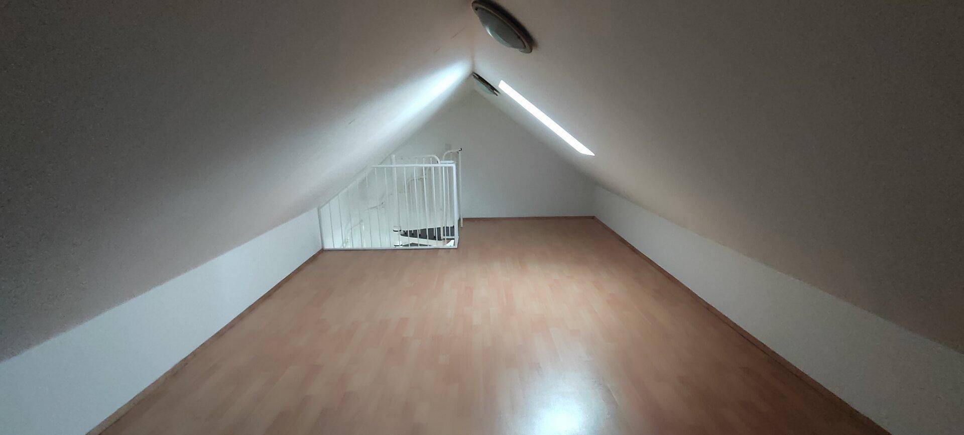 Geräumiger Dachbodenraum mit schrägen Wänden und Laminatboden, ideal als zusätzlicher Wohnraum.