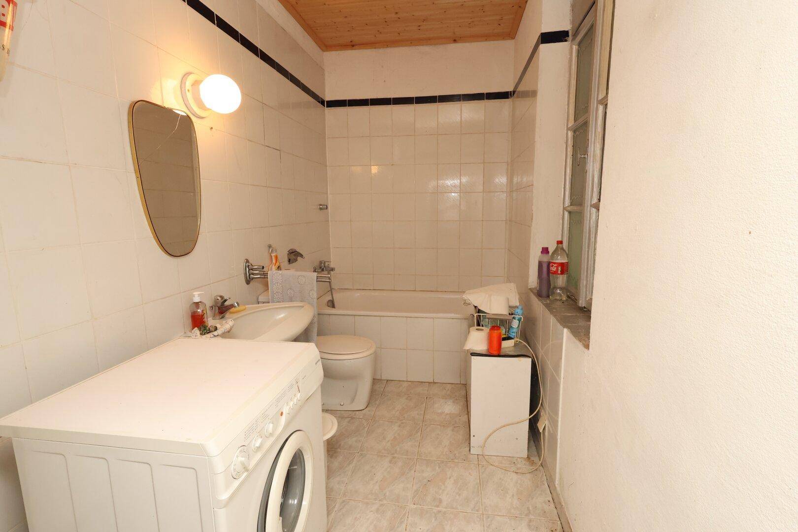 Gefliestes Badezimmer mit Badewanne, Toilette, Waschbecken, Waschmaschine und einem Fenster.
