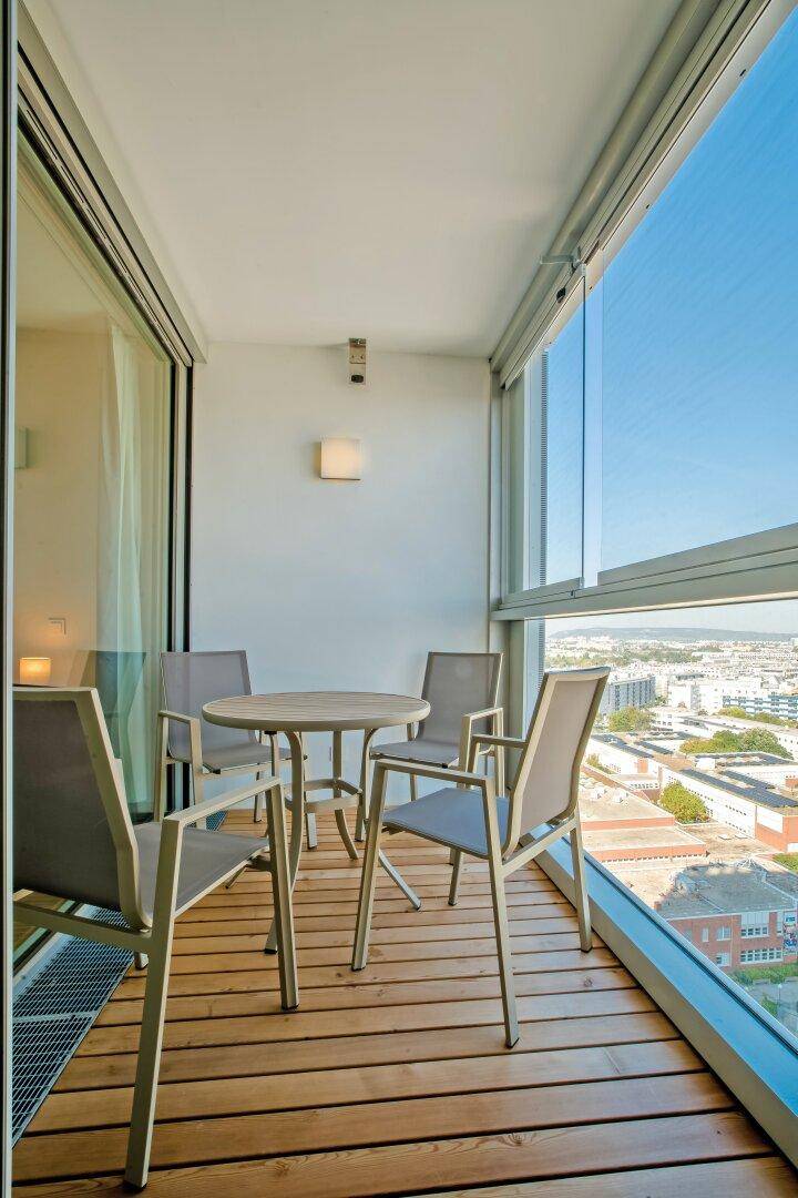 Gemütlicher Balkon mit Holzboden, Sitzgelegenheiten und weitem Blick über die Stadt.