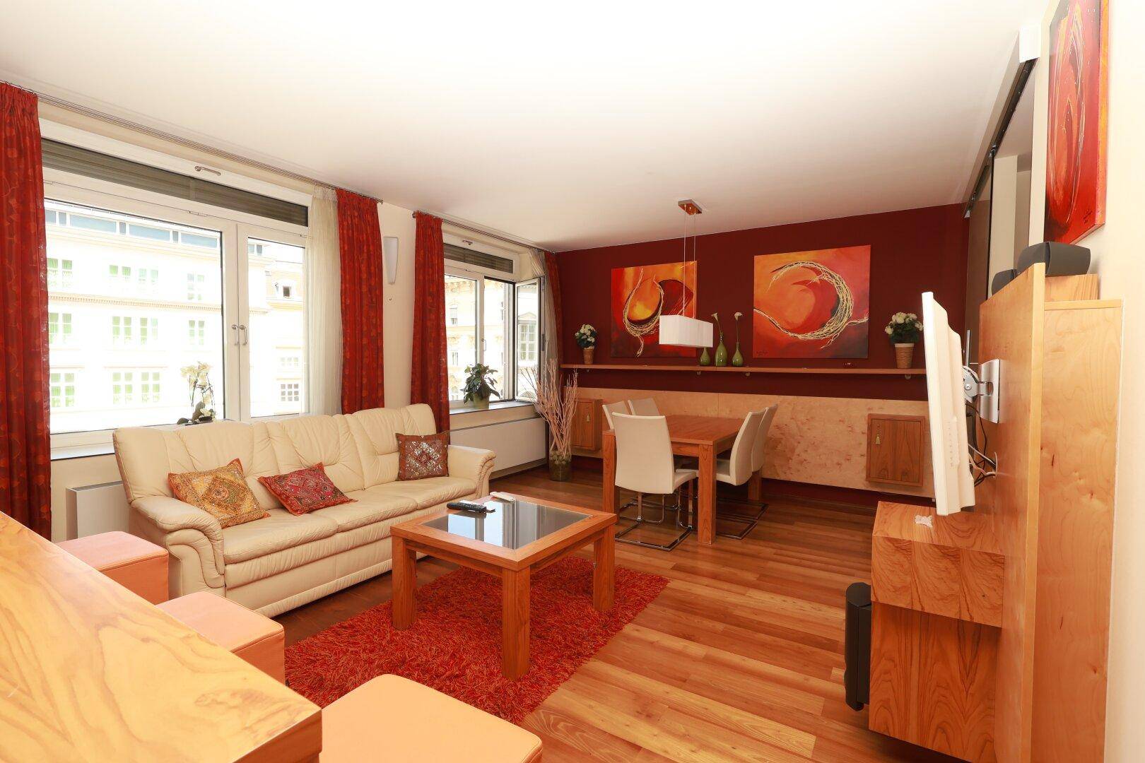 Gemütlicher Wohn- und Essbereich mit Holzboden, beigem Sofa und farbenfroher Wandgestaltung.