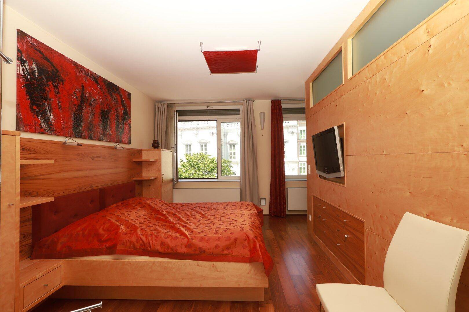 Modernes Schlafzimmer mit Holzbett, Holzboden und roter Bettwäsche sowie Kunst an der Wand.