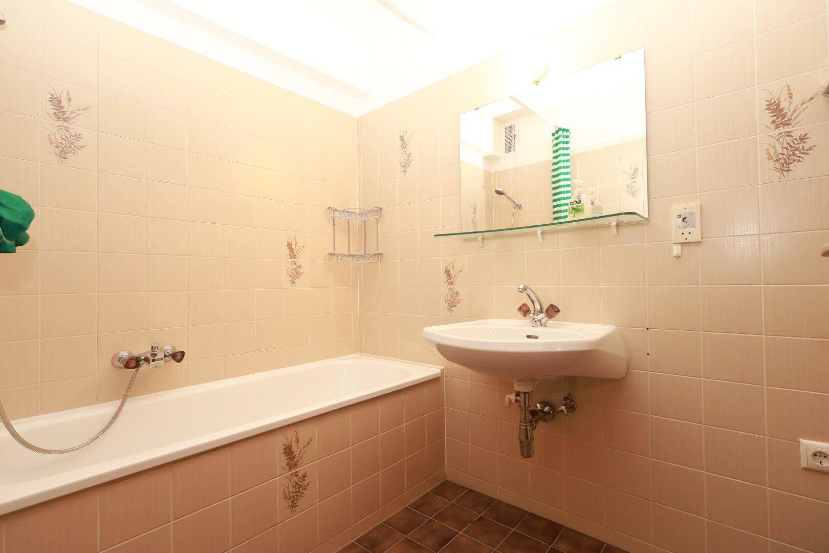Badezimmer mit beigefarbenen Fliesen, Badewanne und Waschbecken, in gutem Zustand.