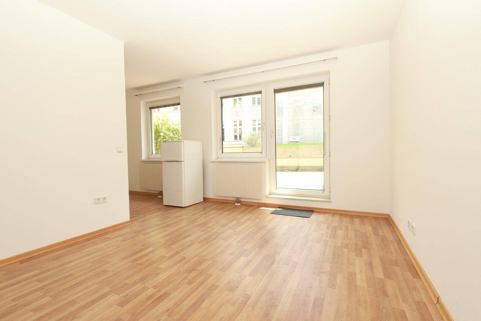 Heller, leerer Raum mit Laminatboden, weißen Wänden und großen Fenstern, ideal als Wohnbereich.