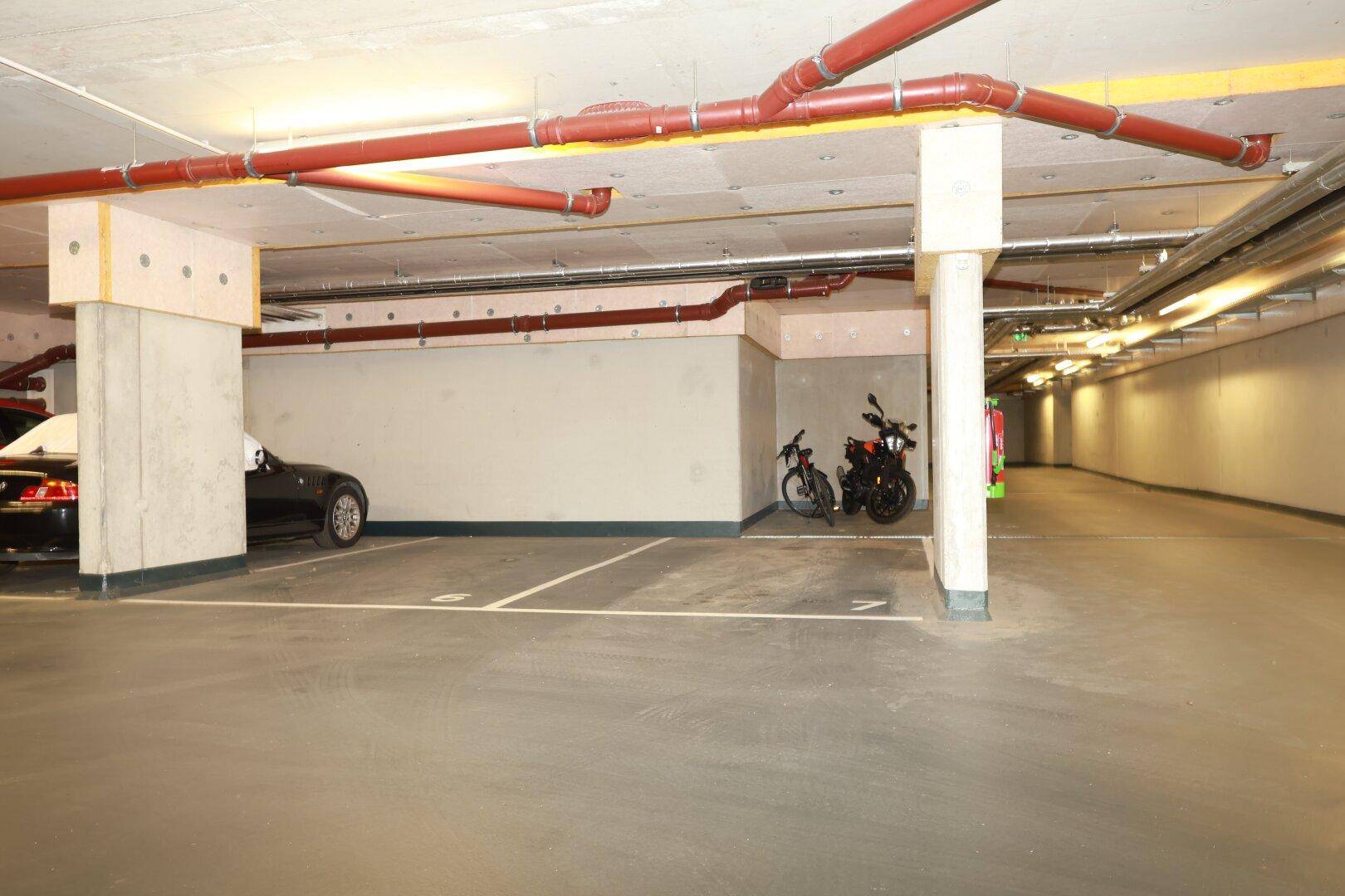 Geräumige Tiefgarage mit markierten Stellplätzen, Fahrrädern und sichtbaren Leitungen an der Decke.
