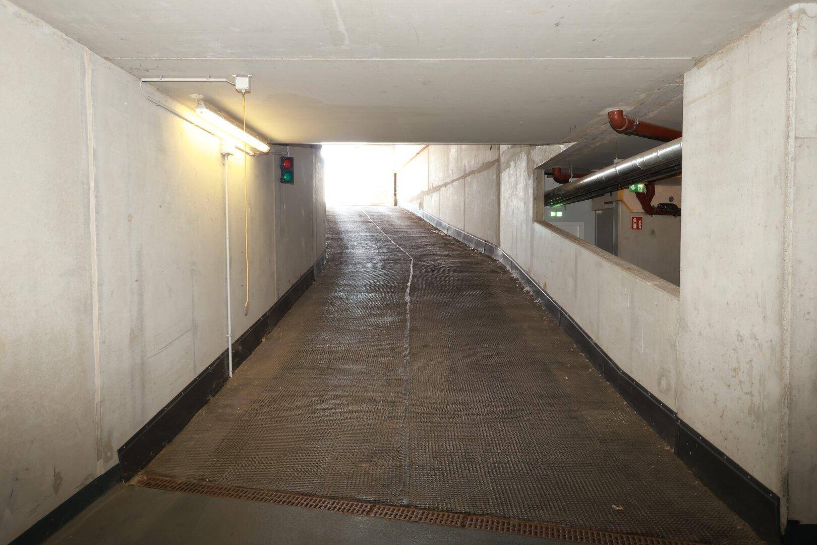 Zufahrtsrampe zur Tiefgarage mit Betonwänden und Ampelsystem am Ausgang.